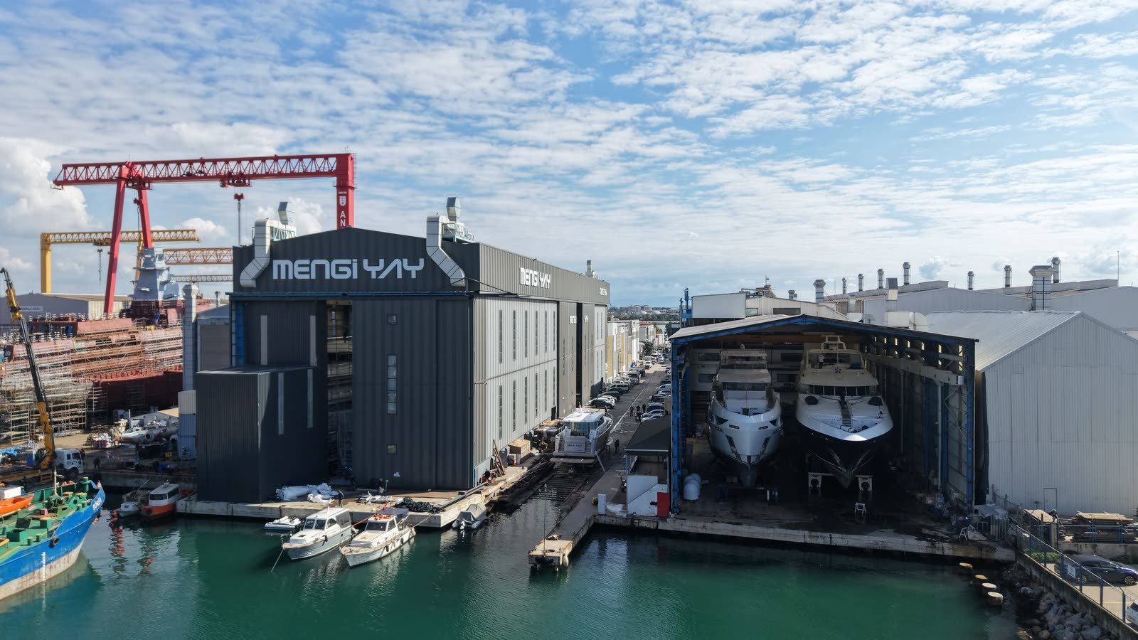 The Mengi Yay building and covered refit hall on the Tuzla waterfront, with two motor yachts standing ashore under the hall roof