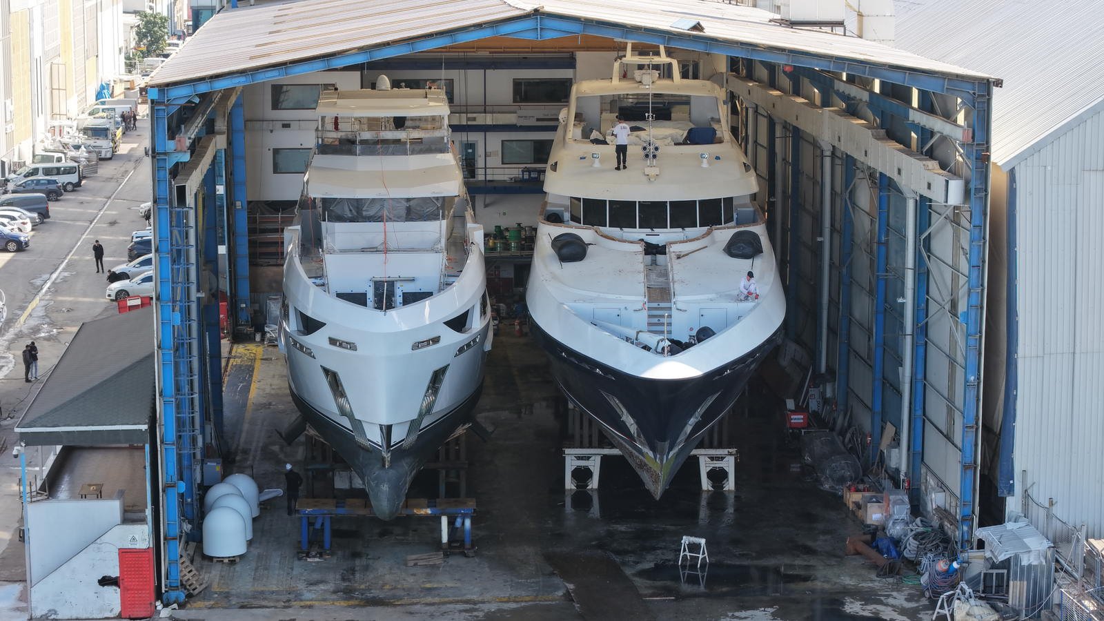 Two motor yachts side by side on their cradles inside a covered refit shed at the Tuzla yard