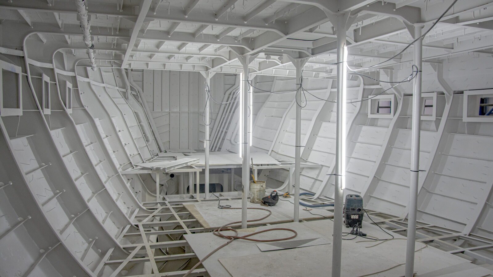 A yacht's interior stripped back to primed frames and stringers, the window apertures standing open in the side