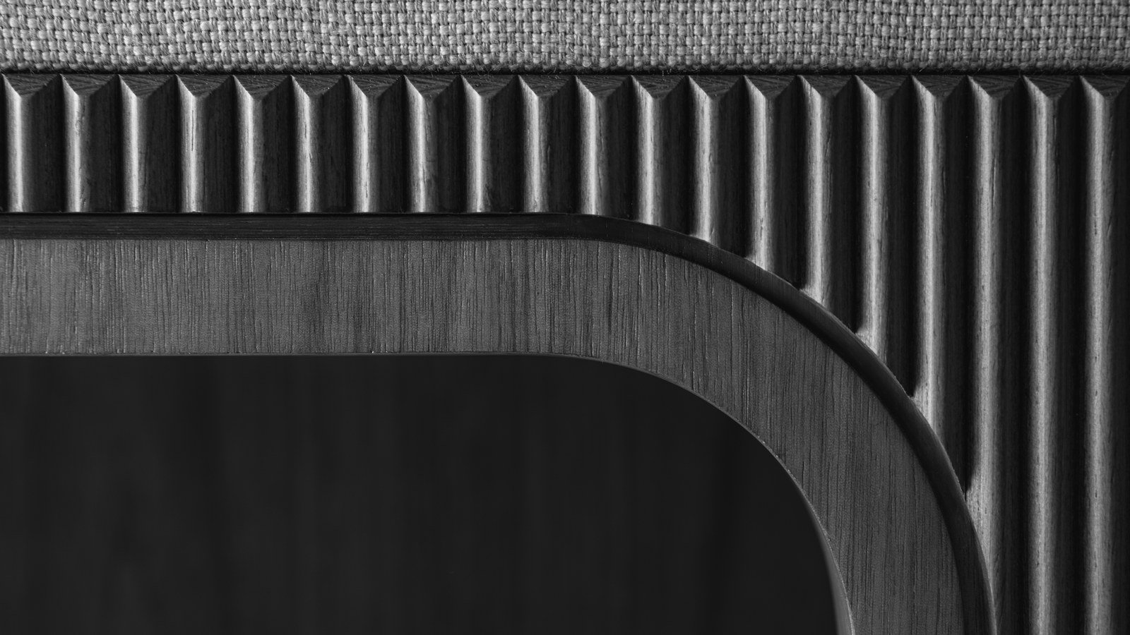 A close view of dark fluted timber joinery meeting a radiused corner detail, with a woven fabric panel above it