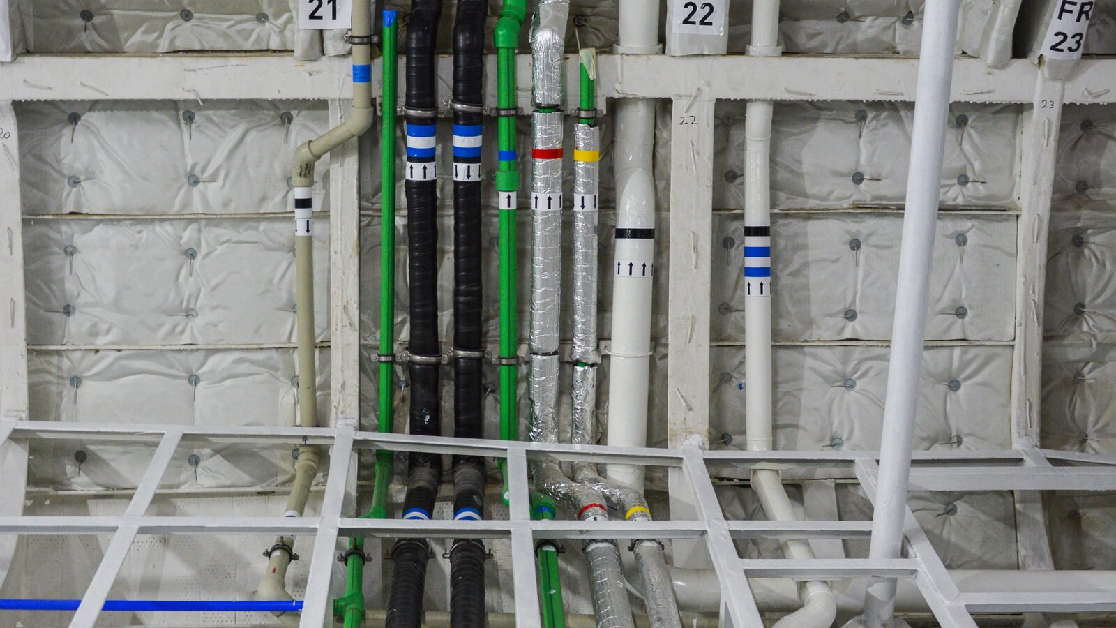 Pipe runs and a cable route crossing numbered frames behind a stripped-out lining, insulation set between the frames