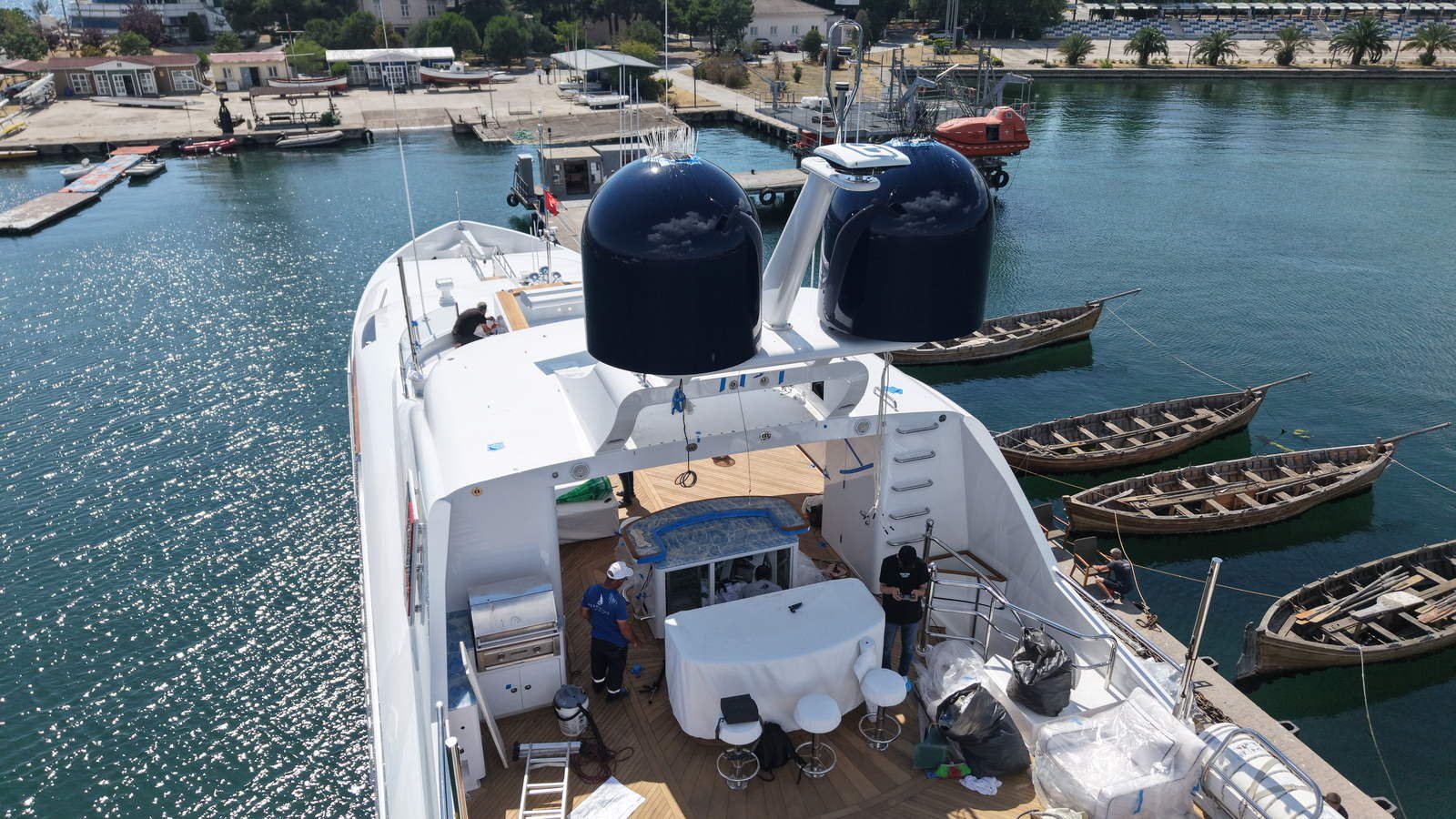 Aerial view of a superyacht sundeck part-way through a yard period, deck furniture still wrapped in protective covering and tools and materials out across the teak while work goes on aft