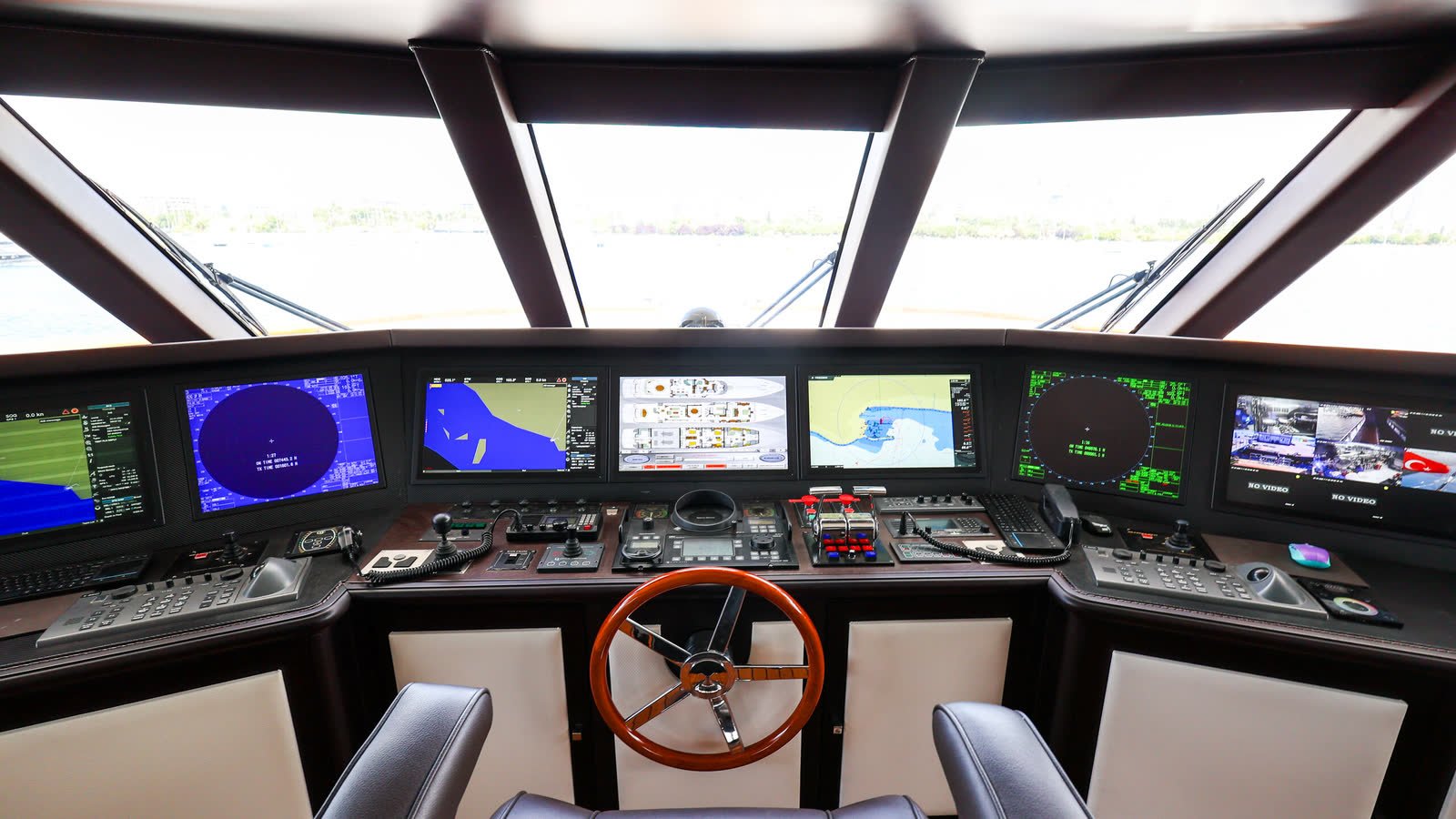 A yacht's bridge with navigation and monitoring displays powered up across the console at the helm.