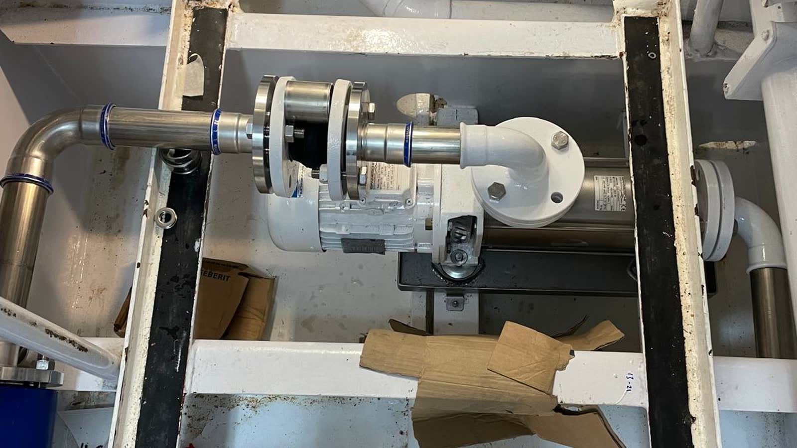 A pump set coupled to stainless flanged pipework on its bed in a compartment, with packaging still on the deck around it.
