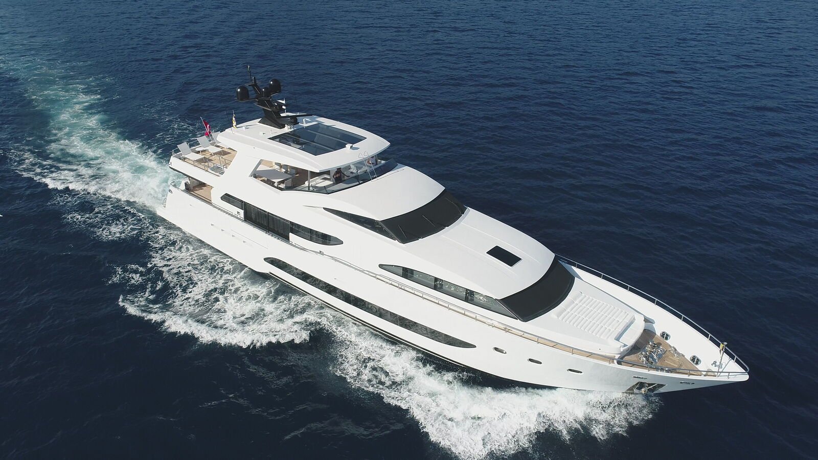 A white motor yacht under way on open water, photographed from the air off her starboard bow with her wake curving astern.