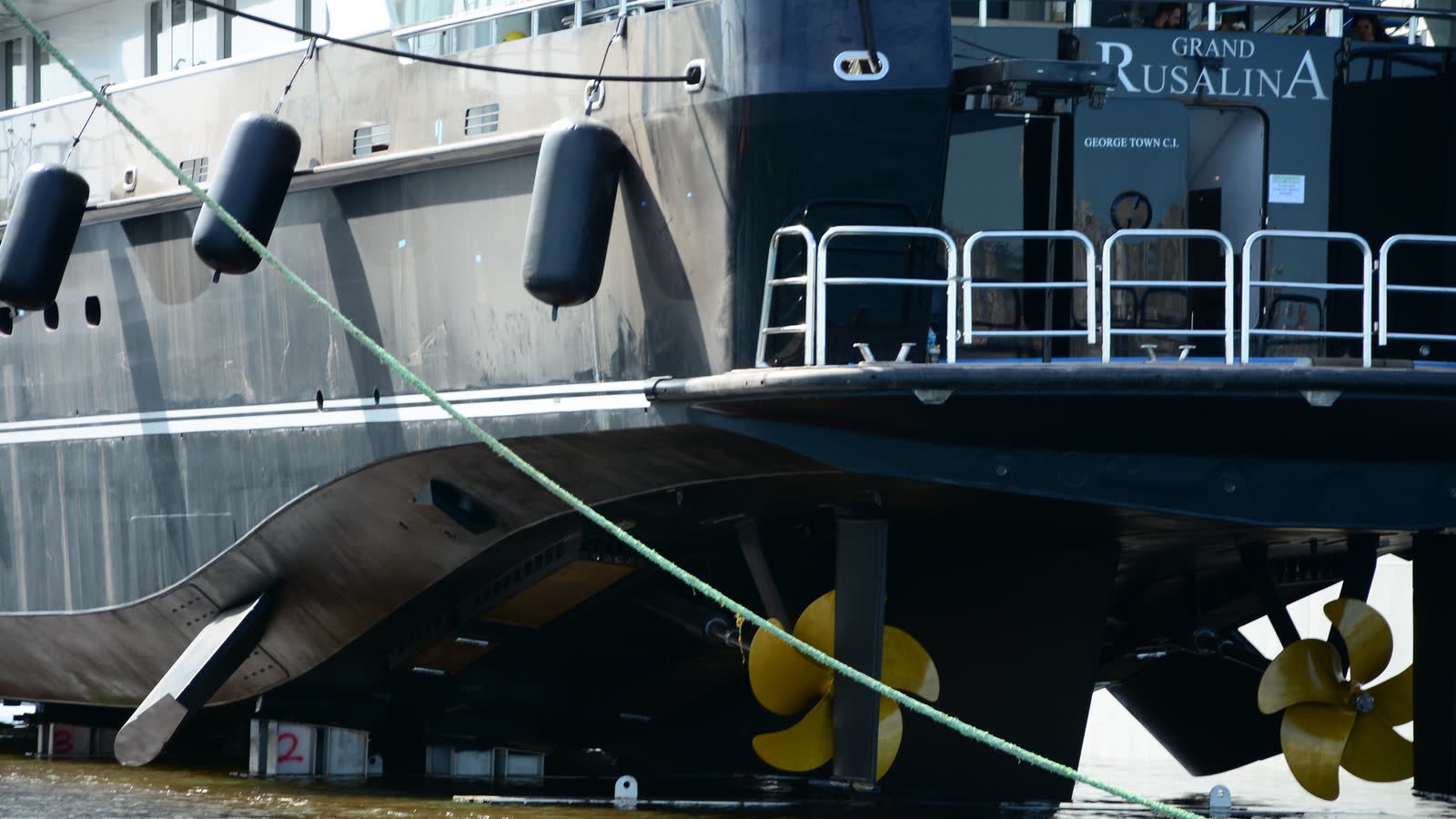 A motor yacht standing on dock blocks with her propellers and shaft struts clear of the water, fenders still rigged along the hull.