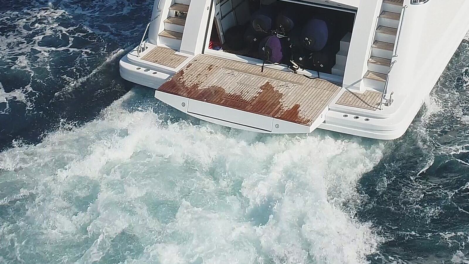 An open transom garage photographed from astern while the yacht is under way, fenders stowed on a rack inside and the bathing platform extended and still wet.
