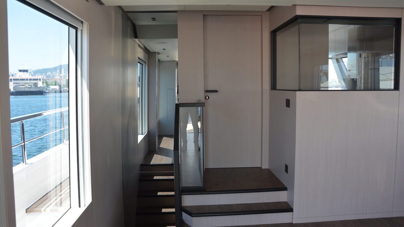A large fixed pane in a yacht side seen from the lobby inside, the water and a far shore beyond it